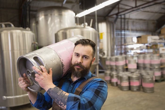 man holding keg on shoulder in brewery 