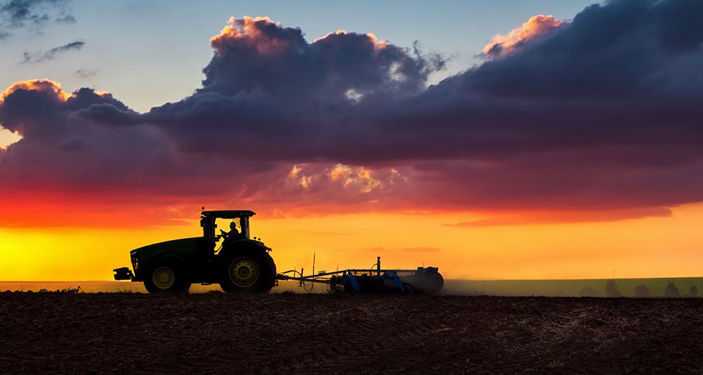 tractor tilling a field at sunset